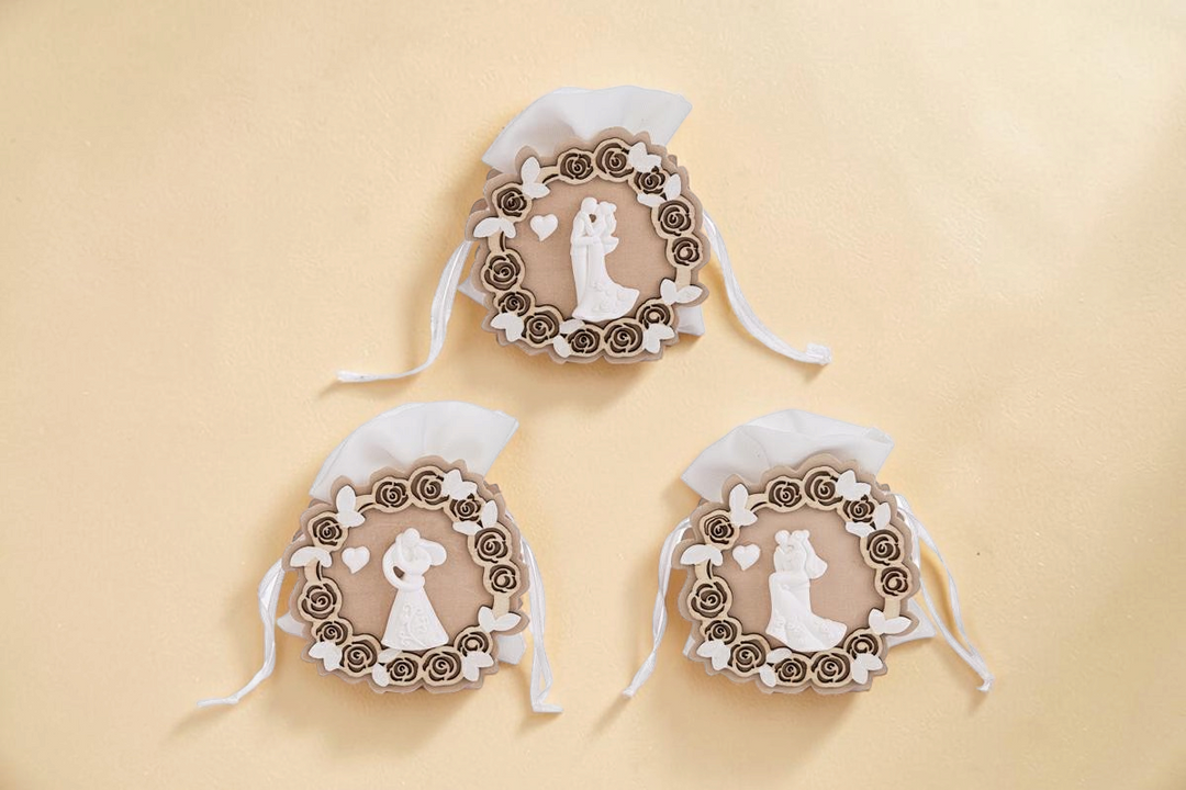 Tre sacchetti portaconfetti La Festa Perfetta in legno con decorazioni a rose, farfalle e statuina sposi bianca