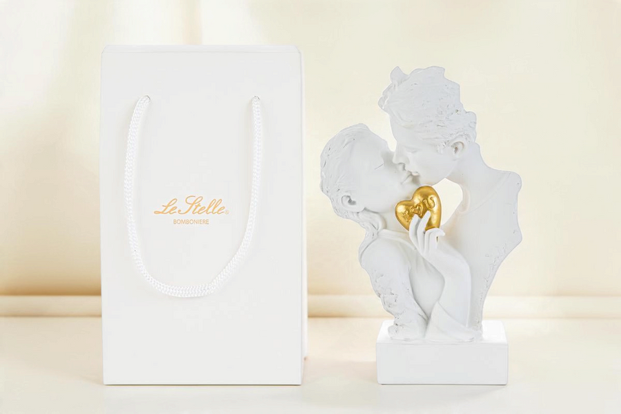 Statua La Festa Perfetta in resina bianca raffigurante una coppia che si bacia con cuore dorato e shopper inclusa